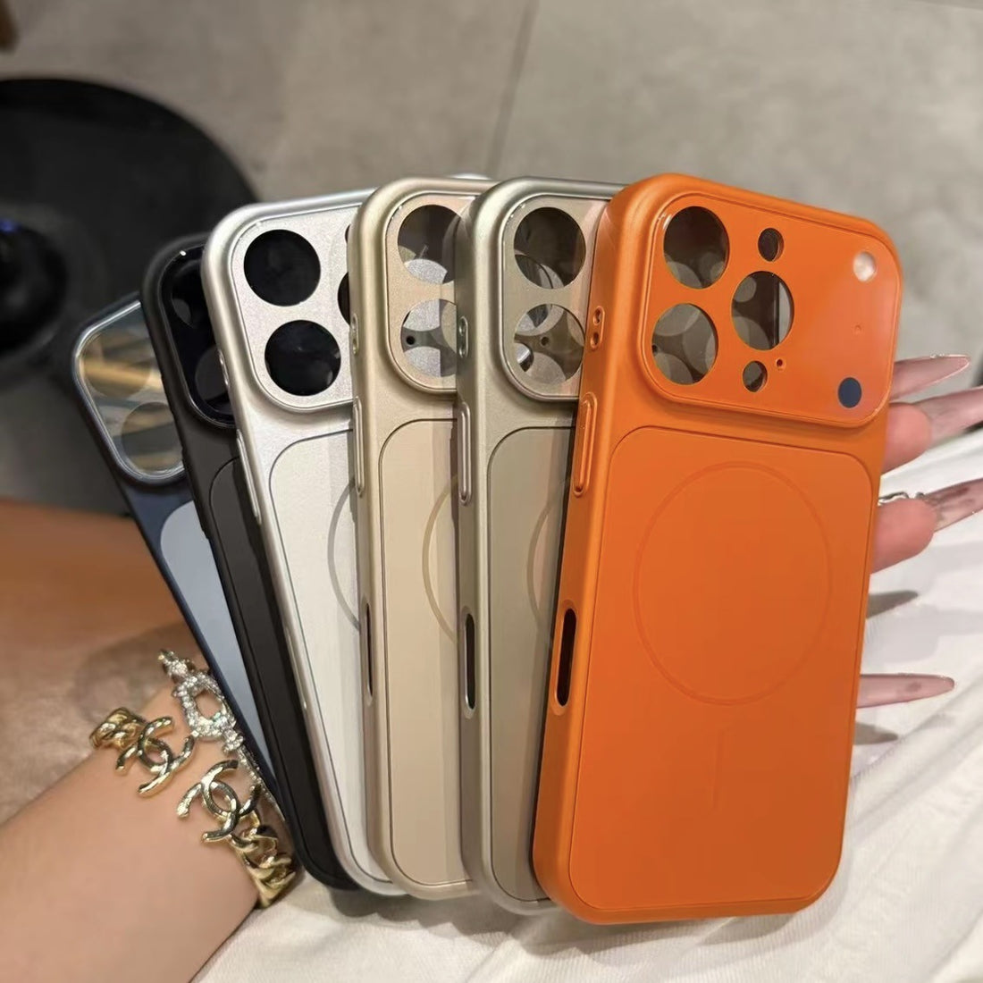 Four phone cases in black, silver, gold, and orange held by a hand.
