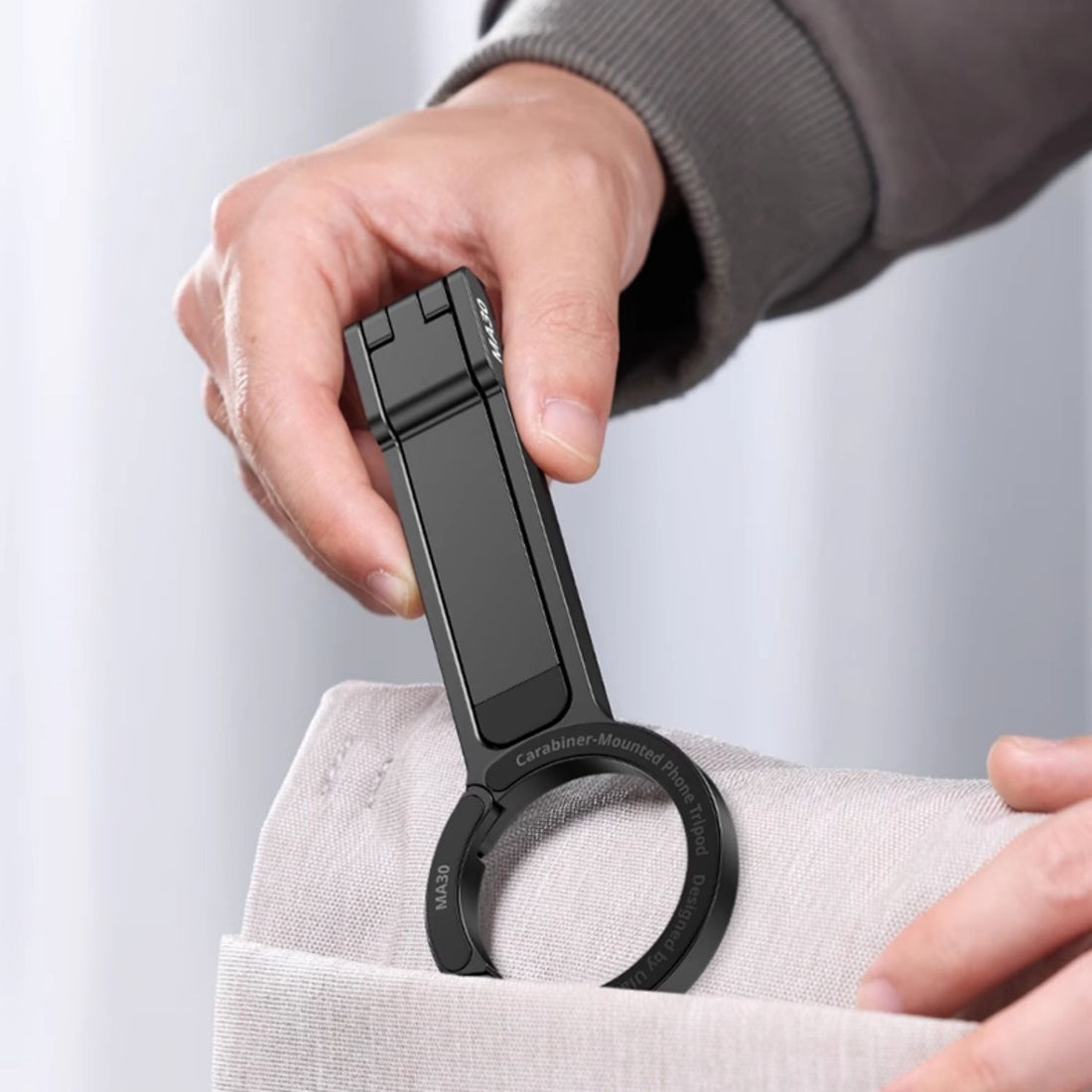 Person using a black carabiner to open a bag on a light gray background